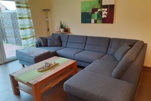 Un salon moderne avec un canapé d’angle gris, une table basse en bois et une plante en pot posée sur une étagère.
