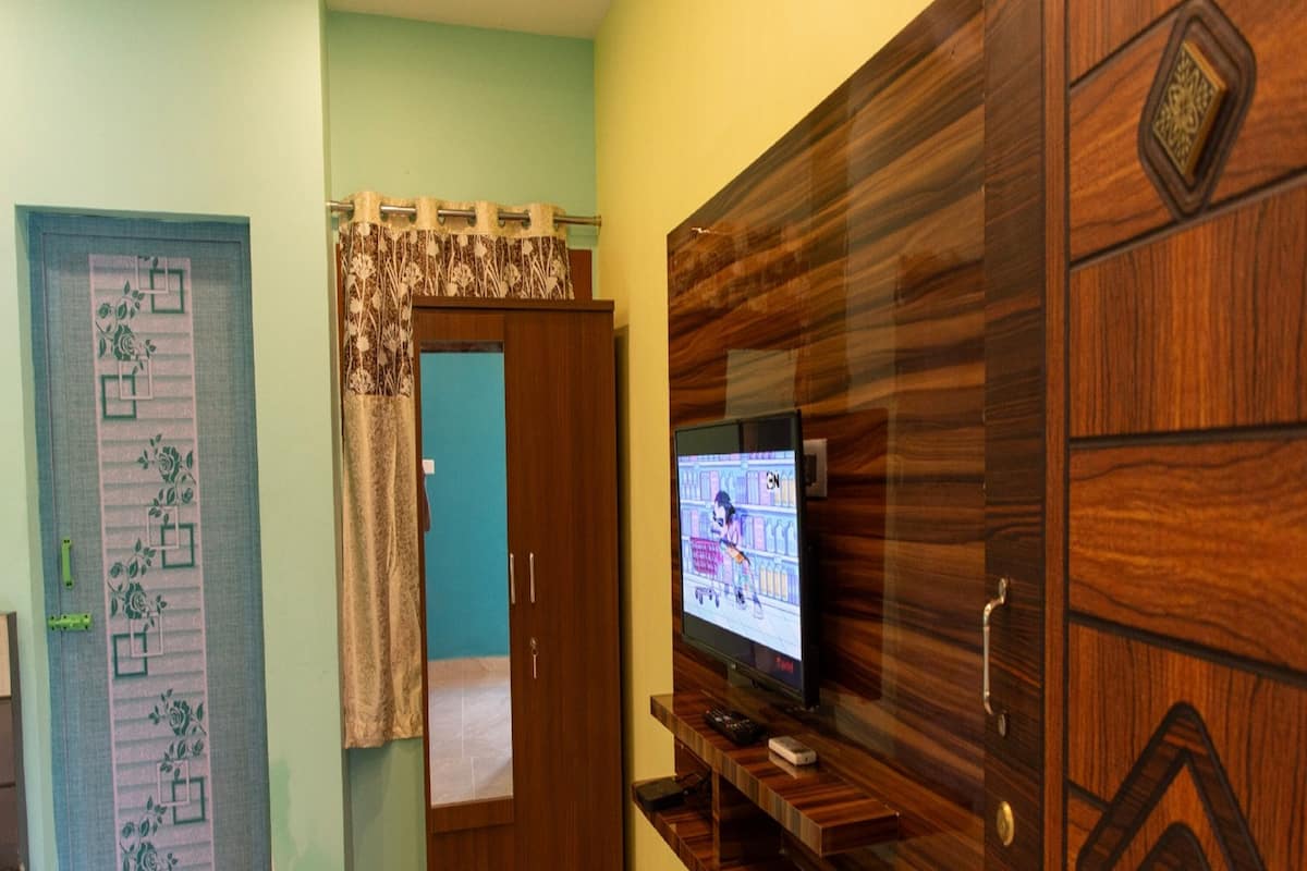 Una habitación con un armario de madera, un televisor fijado en la pared y una puerta con cortinas florales.