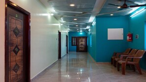 A hallway with a polished tile floor, a wooden door with a geometric design, and a ceiling fan. - Bala Residency  (Puducherry)
