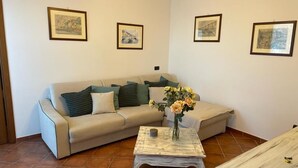 Un salón con un sofá beige, una mesa de centro con un jarrón de flores y cuadros en las paredes.
