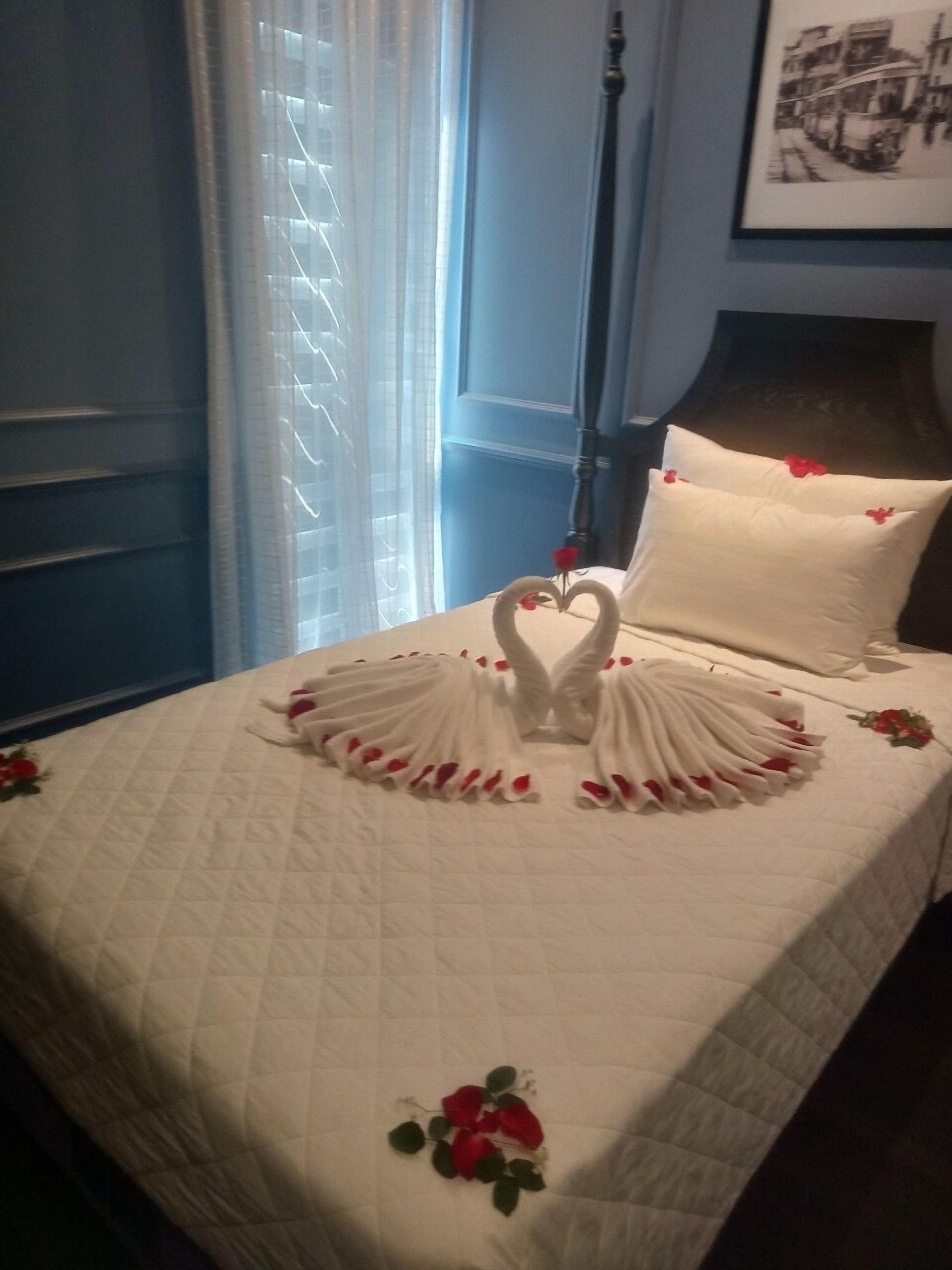 A bed with a white quilt and a heart-shaped towel arrangement.