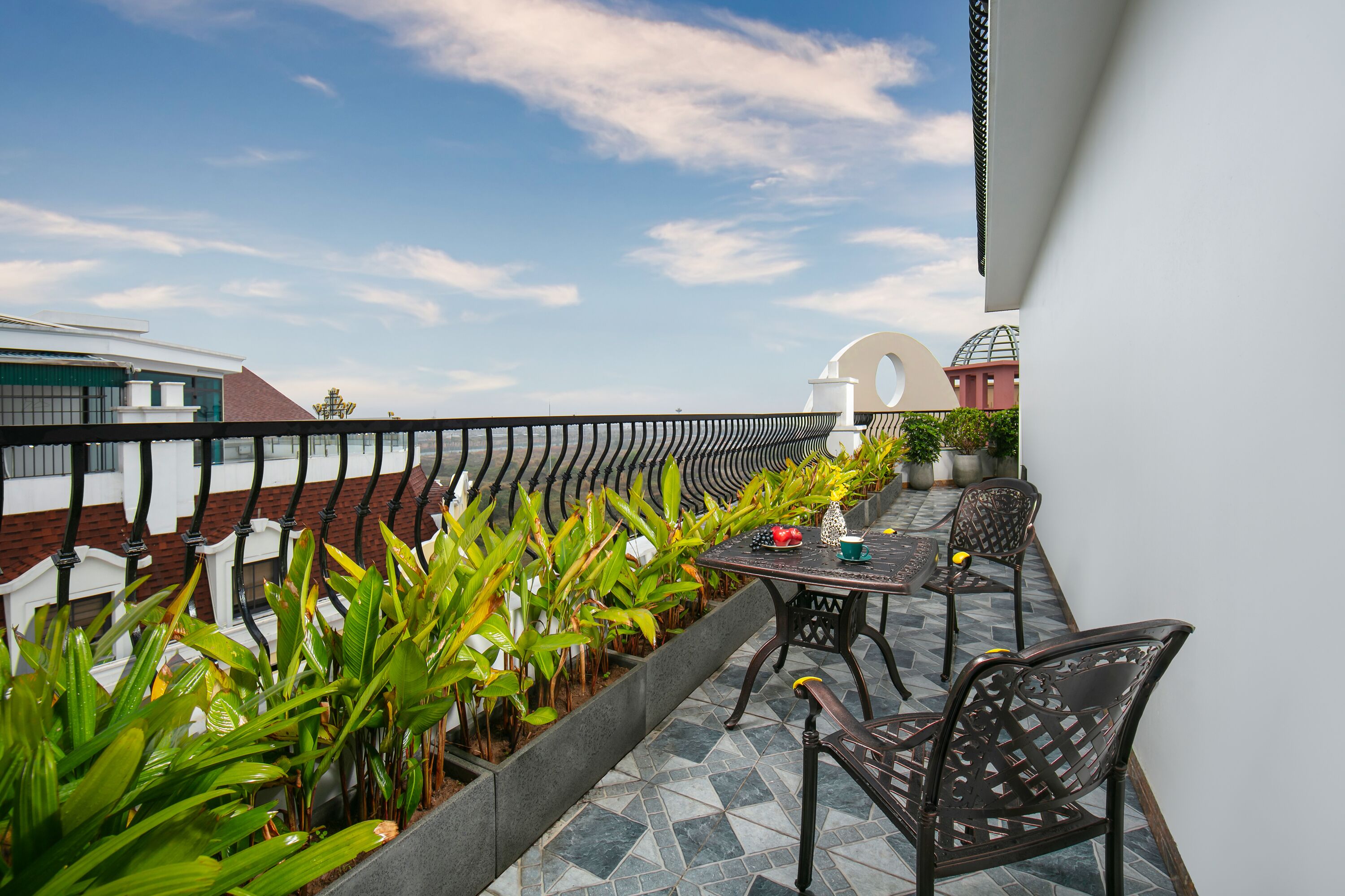 A rooftop terrace with a table and chairs, surrounded by potted plants and a view of a building with a dome.