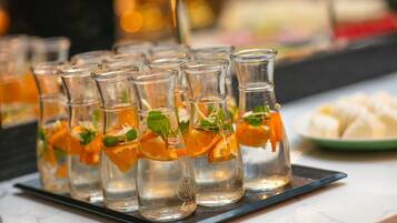 A row of clear glass bottles with orange slices and mint leaves, placed on a black tray.