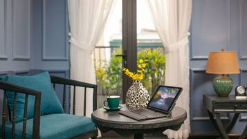 Ein Zimmer mit einem petrolfarbenen Sofa, einem kleinen runden Tisch mit einem Laptop, einer Vase mit gelben Blumen, einer grünen Tasse und einer Lampe.