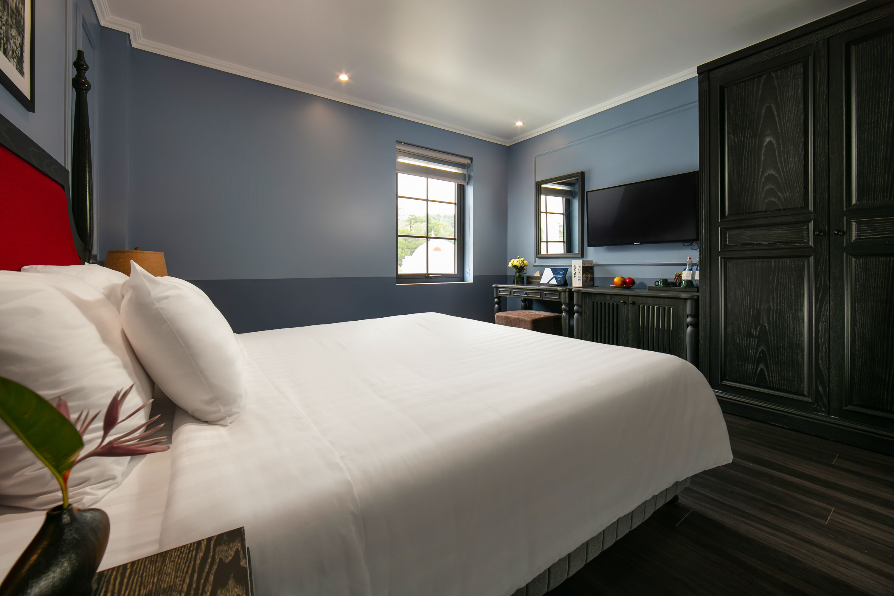 A bedroom with a large bed, a dresser, a television, and a window.