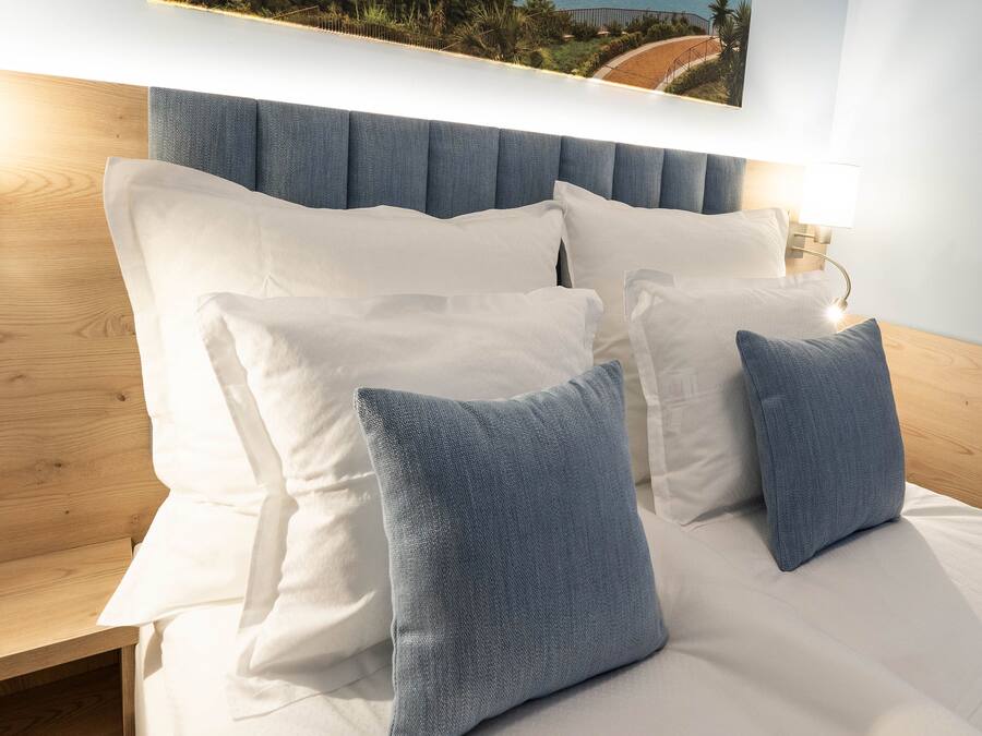 A neatly made bed with white and blue pillows, a wooden headboard, and wall-mounted lights.