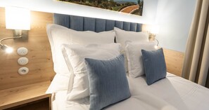 Un lit bien fait, avec des oreillers blancs et bleus, une tête de lit en bois et des lampes fixées au mur.