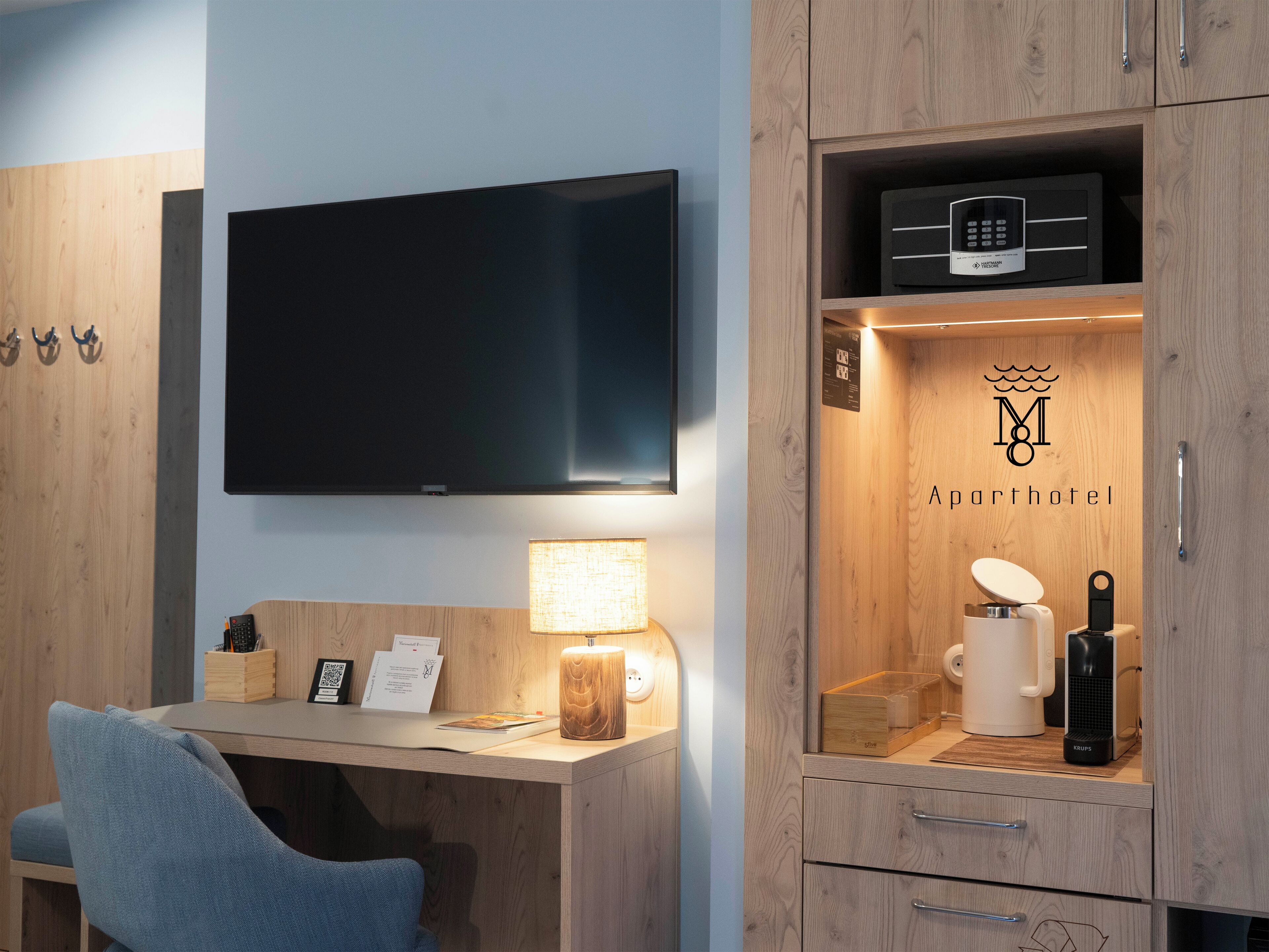 A modern hotel room with a flat-screen TV, a desk with a lamp, a minibar, and a coffee maker.