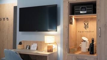 A modern hotel room with a flat-screen TV, a desk with a lamp, a minibar, and a coffee maker.