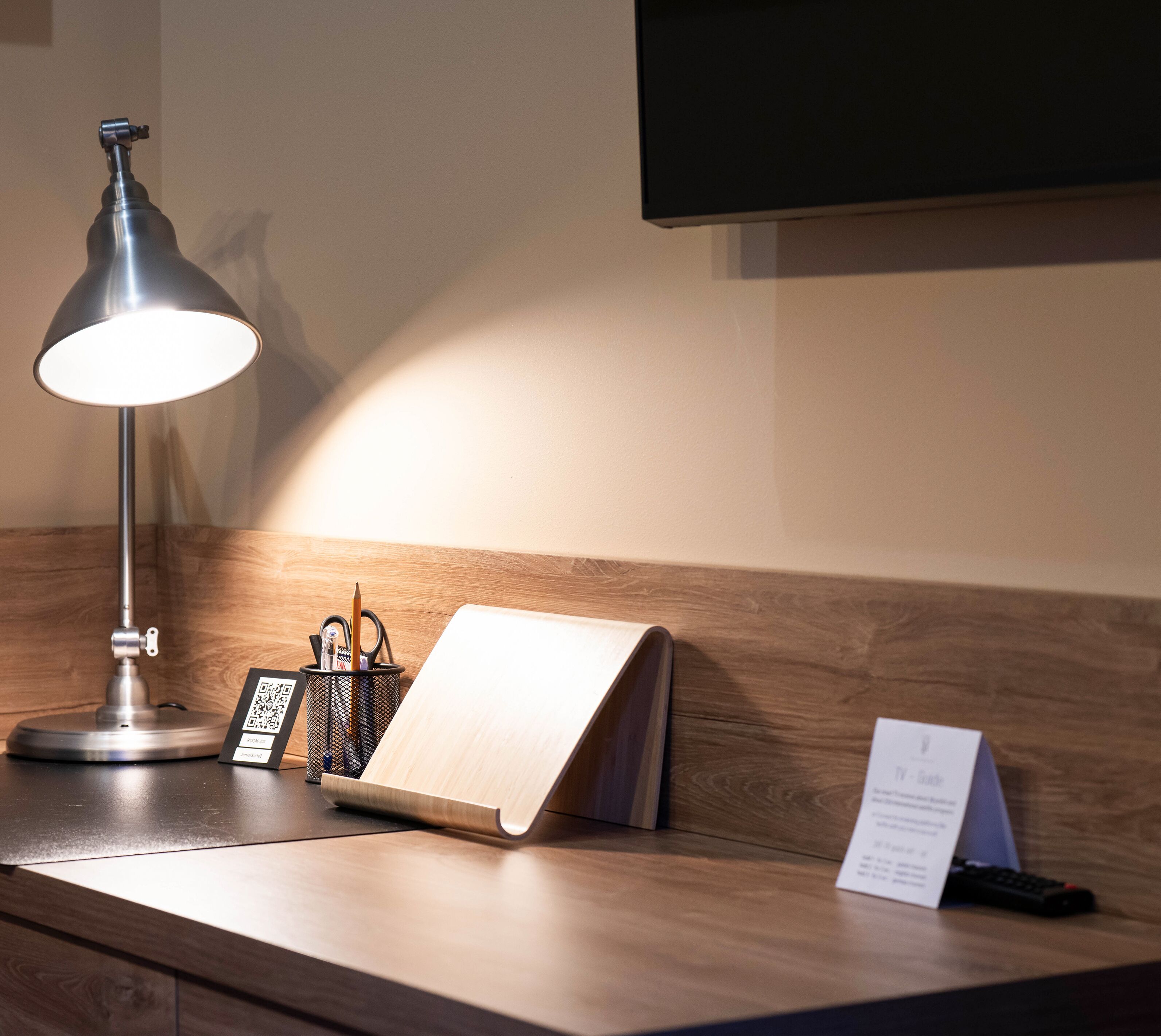 Una scrivania con lampada da tavolo, un blocco note, un portapenne e un telecomando per la TV.