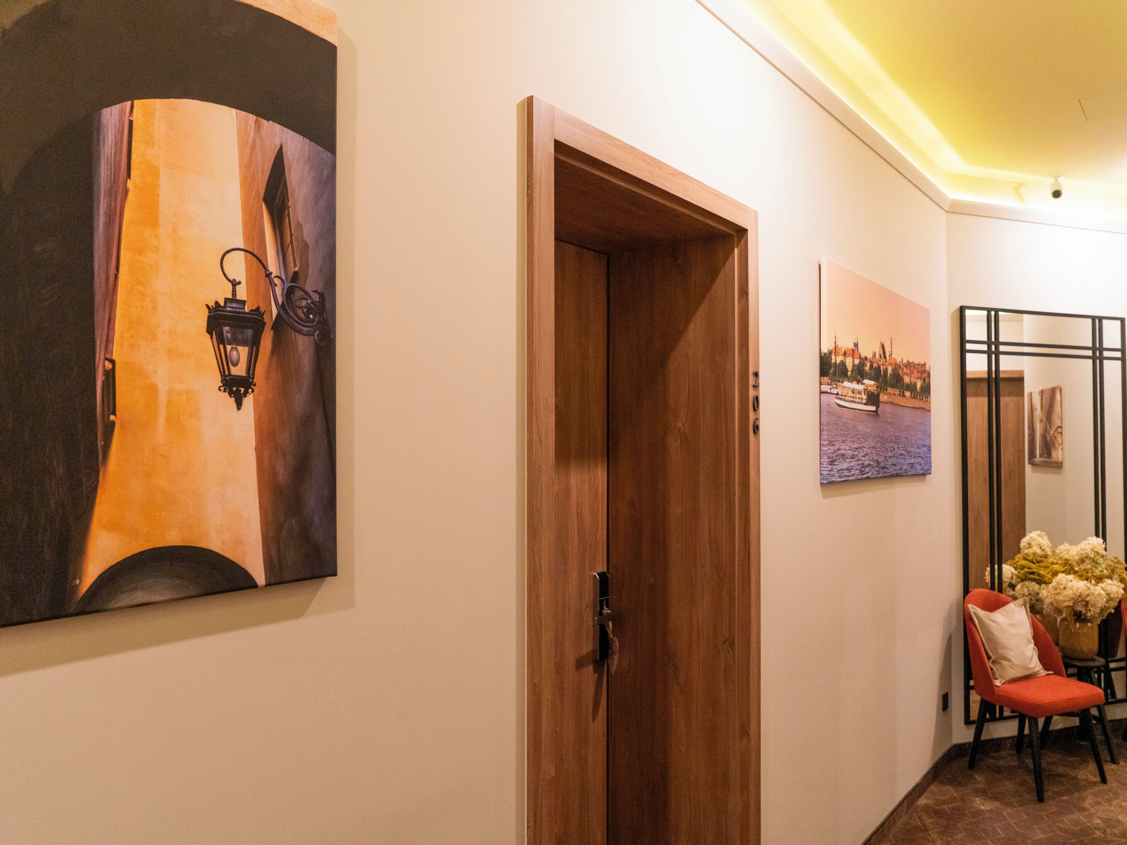 Un pasillo con una puerta de madera, una lámpara fijada a la pared y un cuadro enmarcado.