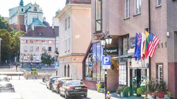 A street view with parked cars, a building with a sign 'P', and flags.
