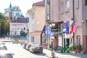 Une vue de rue avec des voitures garées, un bâtiment portant une enseigne « P » et des drapeaux.