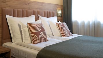 Un lit bien fait, avec une tête de lit en bois, une literie blanche et des coussins à motifs.