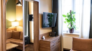 Een hotelkamer met een bank, een televisie, een houten dressoir, een plant en een raam met gordijnen.