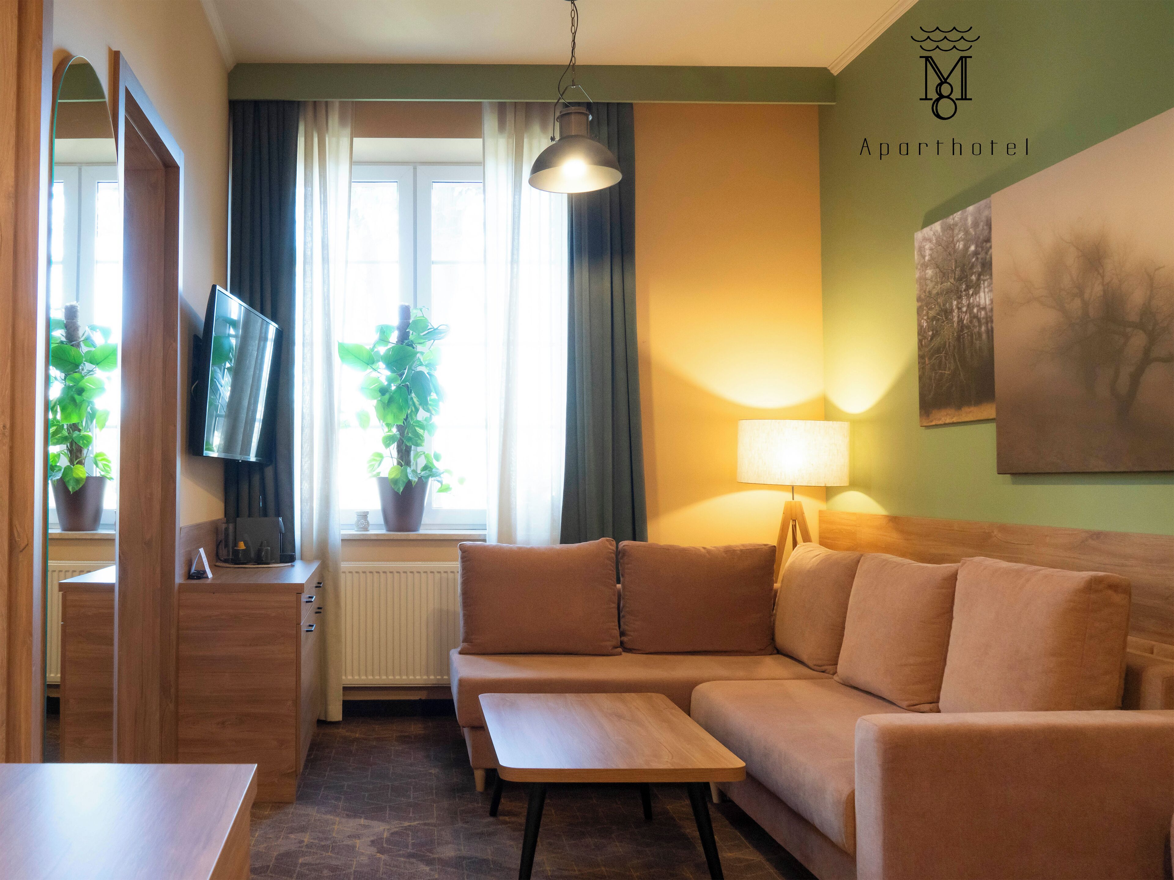 Ein modernes Hotelzimmer mit einer Couch, einem Holztisch, einem Fernseher, einer Lampe und zwei Zimmerpflanzen.
