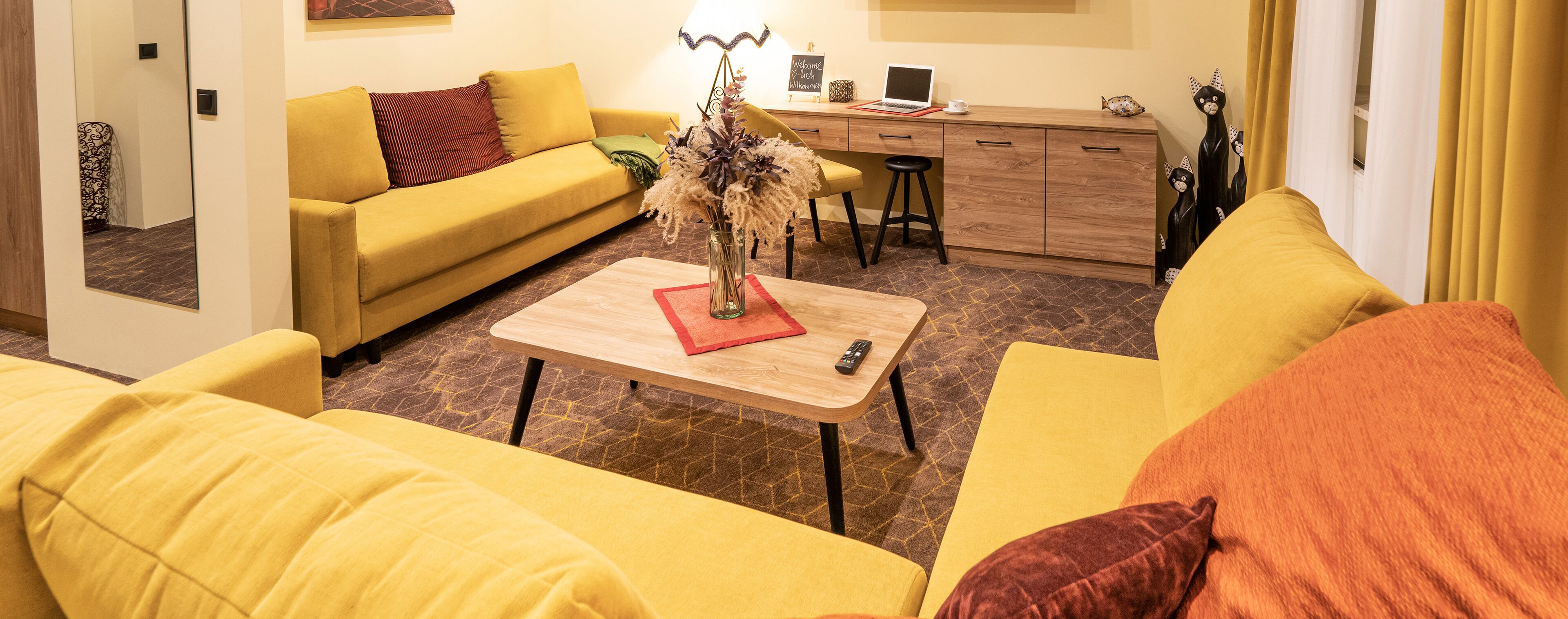 Un canapé jaune, une table basse en bois et un bureau avec un ordinateur portable, le tout dans un espace de vie.