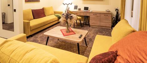 Un canapé jaune, une table basse en bois et un bureau avec un ordinateur portable, le tout dans un espace de vie.