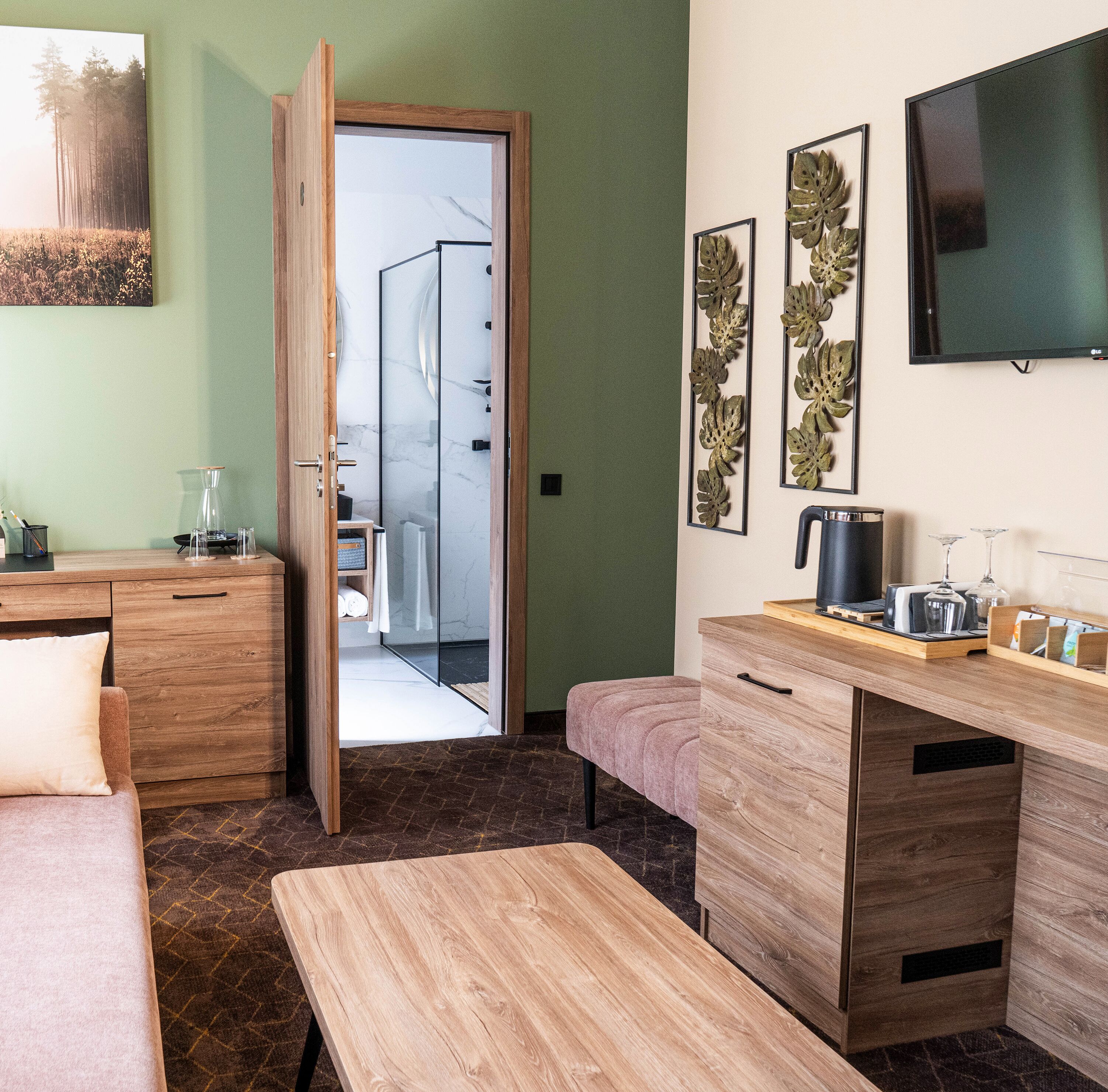 Quarto moderno com escrivaninha de madeira, um banco, chuveiro de vidro e televisão na parede.