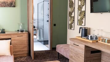 Quarto moderno com escrivaninha de madeira, um banco, chuveiro de vidro e televisão na parede.