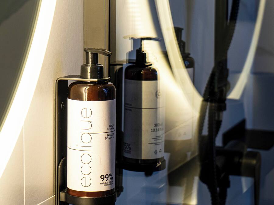 A bathroom with a mirror, a bottle of body lotion, and a hand soap dispenser.