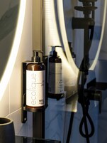 A bathroom with a mirror, a bottle of body lotion, and a hand soap dispenser.