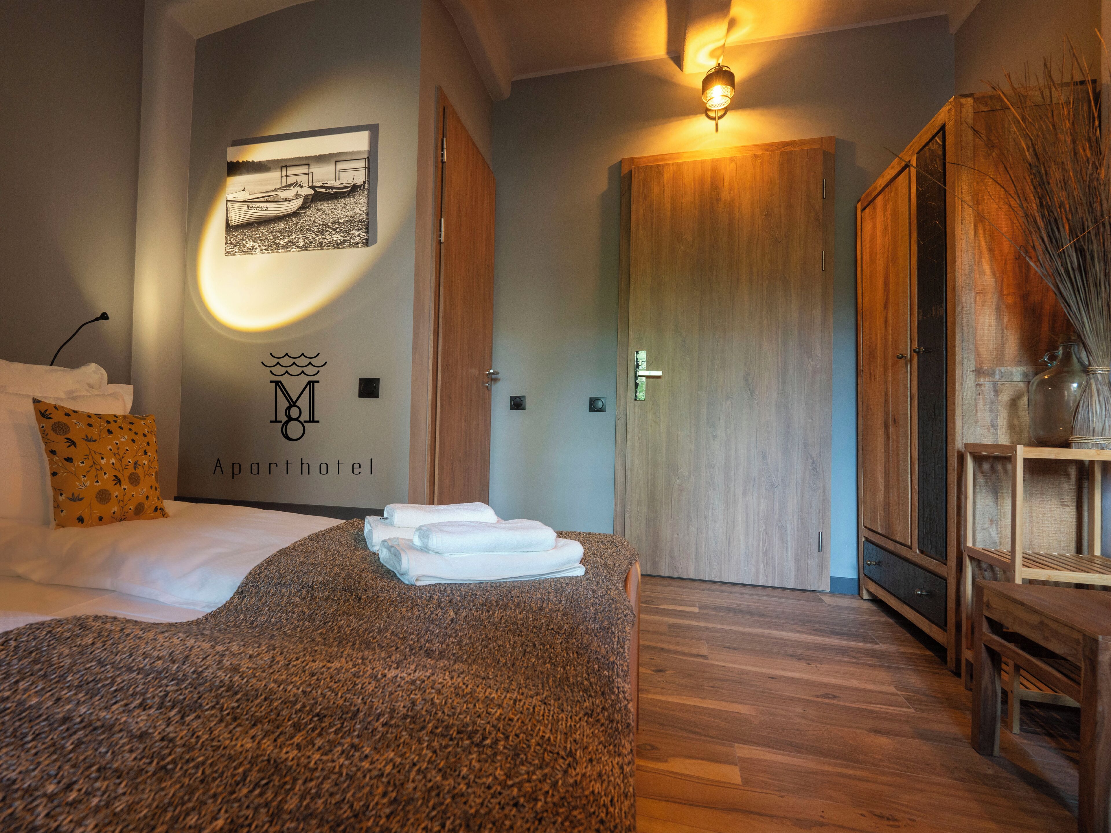 A hotel room with a bed, a wall-mounted picture, a wooden wardrobe, and a bedside table.