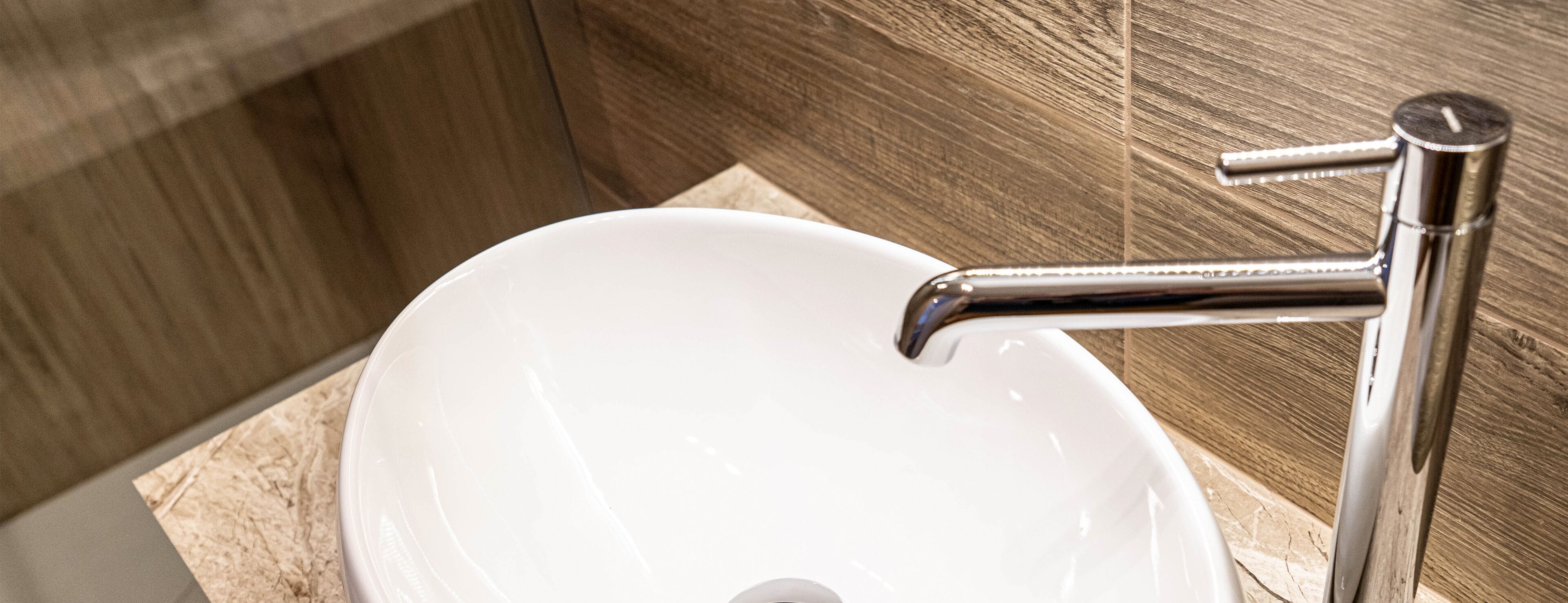 Ein weißes Waschbecken mit Armatur aus Chrom in einem Badezimmer mit Holzvertäfelung.