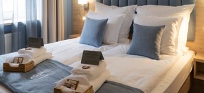 Un lit bien fait, avec du linge de lit blanc, des oreillers bleus et une table de chevet sur laquelle se trouve une lampe.
