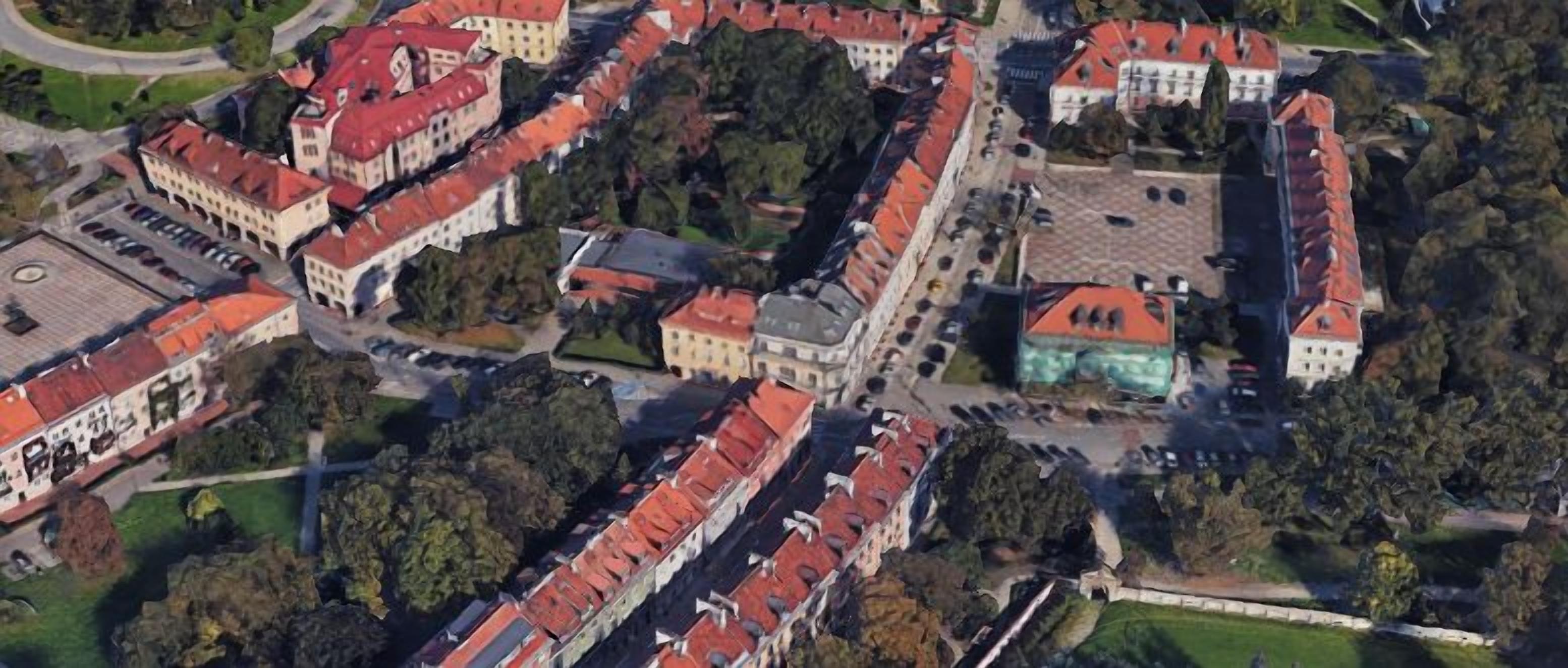 Vista aérea de un pueblo histórico con edificios de tejados rojos, una iglesia destacada y un área de estacionamiento.
