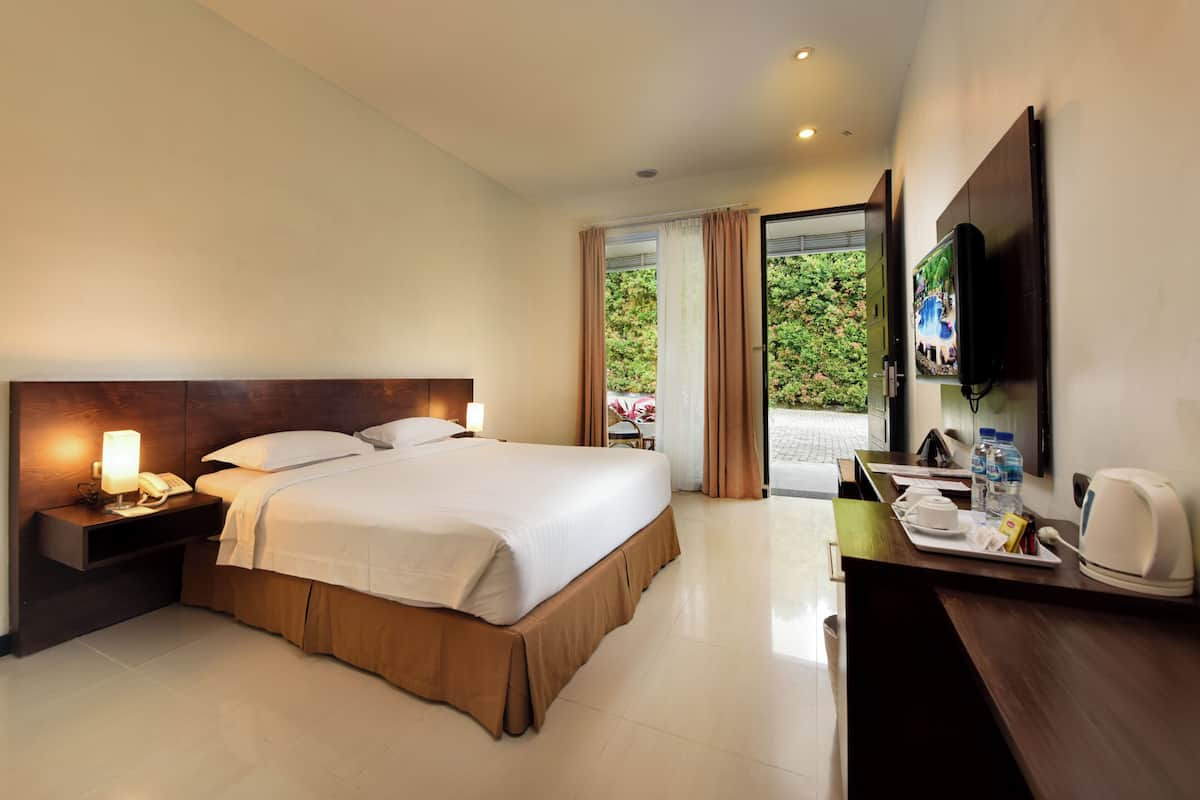 A hotel room with a large bed, a bedside table with a lamp, a TV mounted on the wall, and a desk with a tray of breakfast items.