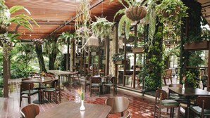 Un restaurant intérieur avec des tables et des chaises en bois, entouré d’une végétation luxuriante et agrémenté de plantes suspendues.