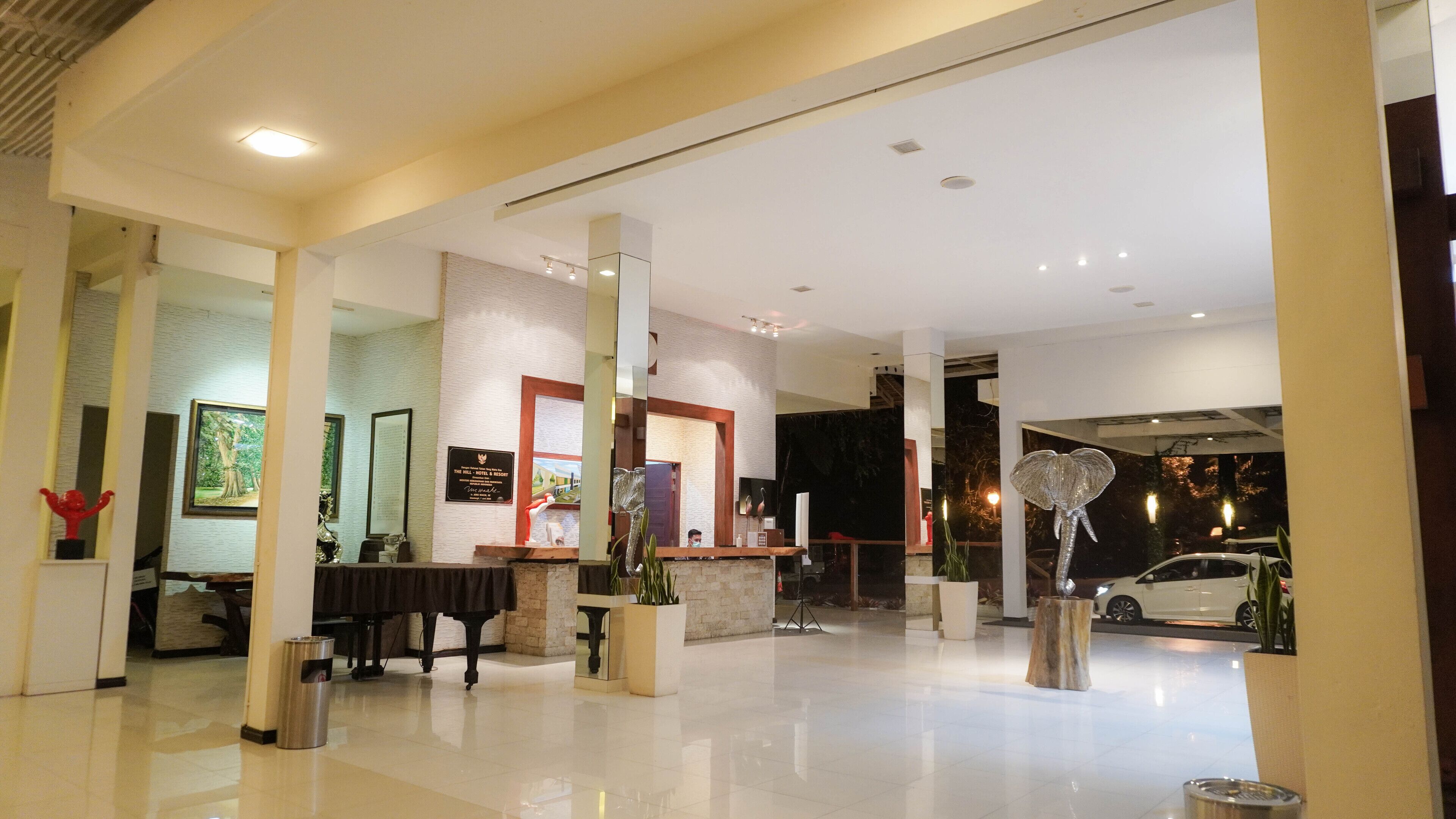 A spacious lobby with a reception desk, a piano, and a large mirror.