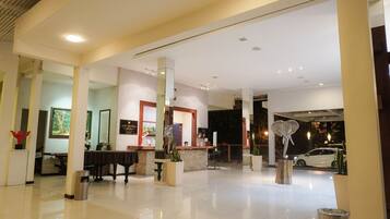 A spacious lobby with a reception desk, a piano, and a large mirror.