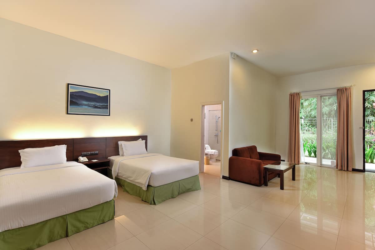 A hotel room with two beds, a sofa, a small table, and a bathroom visible through an open door.