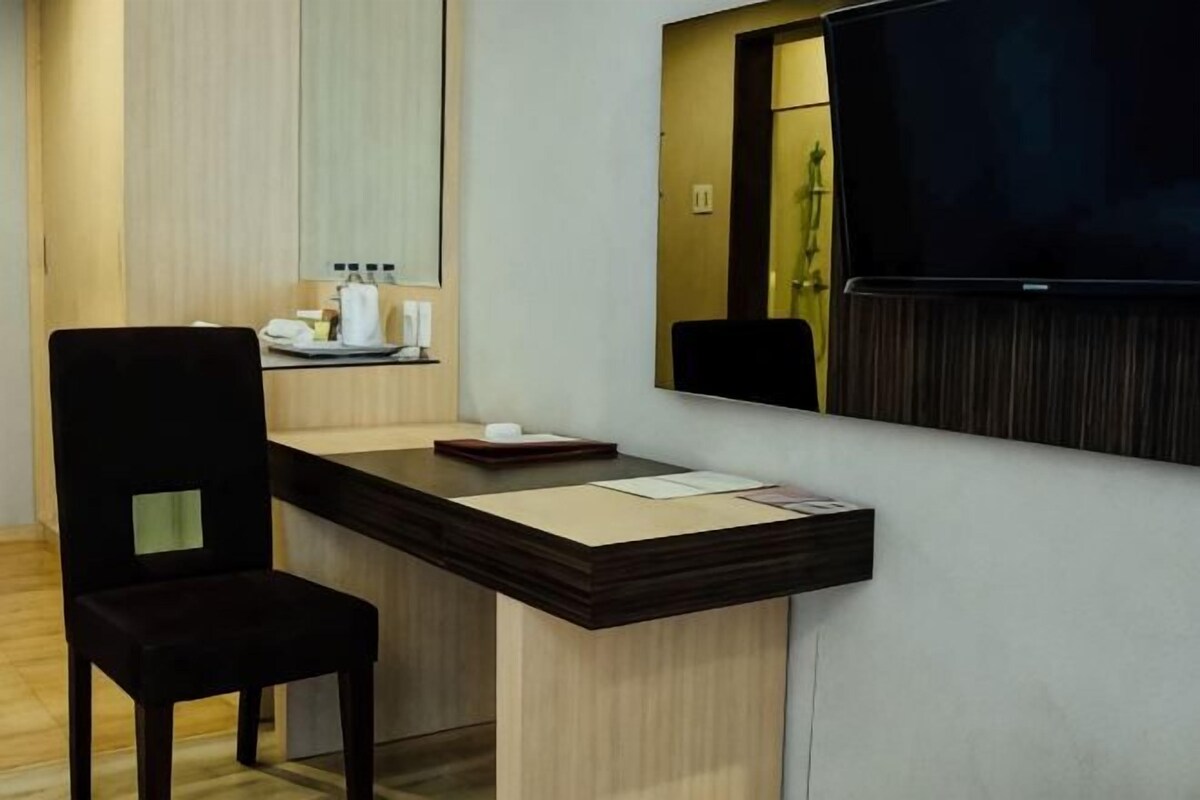 Une chambre d’hôtel équipée d’un bureau, d’une chaise, d’un téléviseur à écran plat, d’un miroir et d’une petite étagère contenant des articles de toilette.