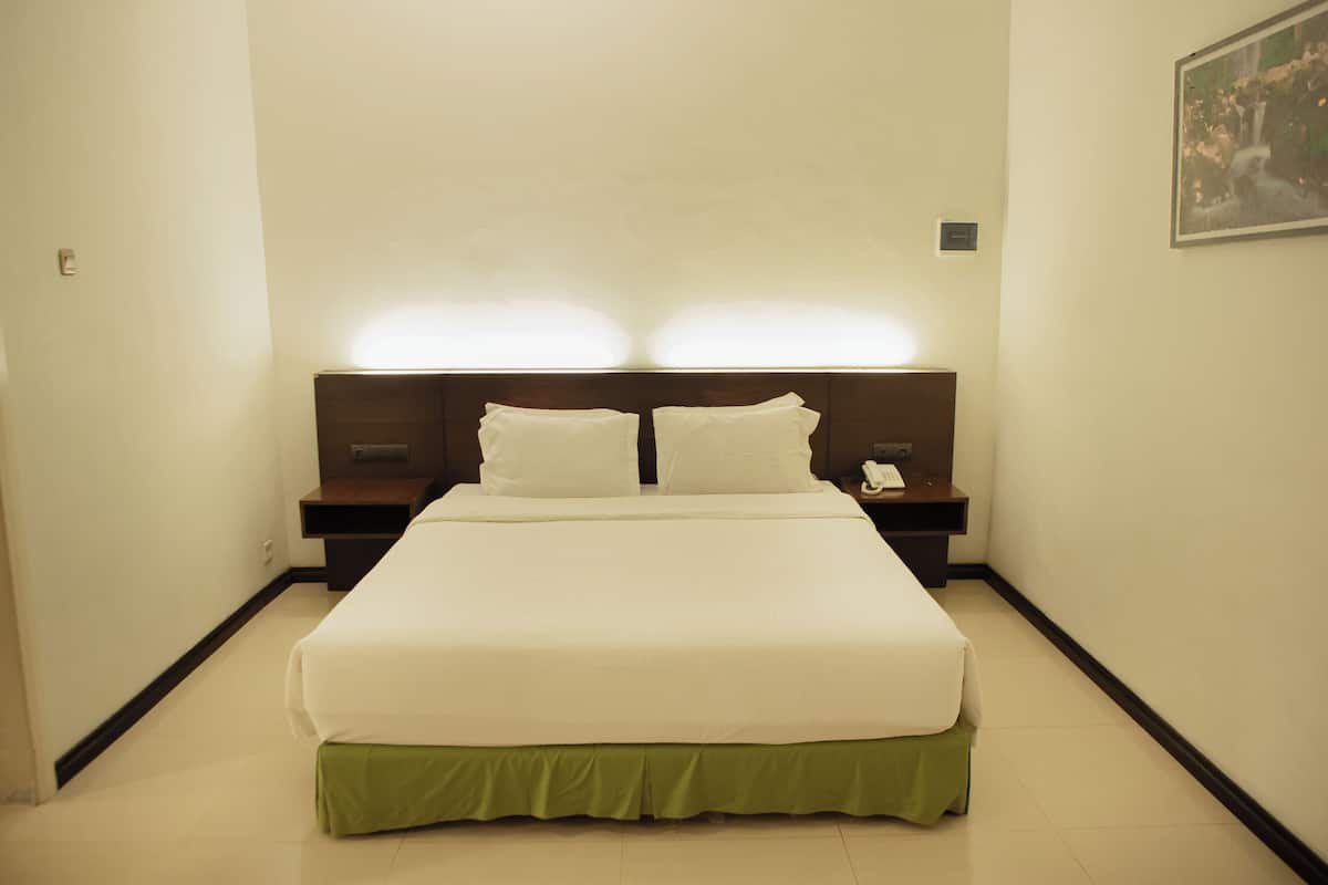 A hotel room with a large bed, two bedside tables, a nightstand, and a wall-mounted telephone.
