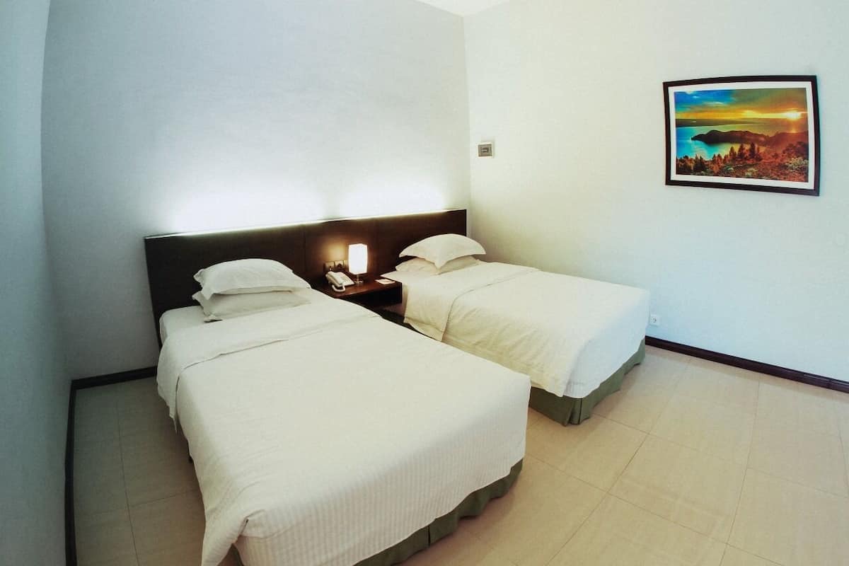 A hotel room with two beds, a nightstand with a lamp, and a framed picture on the wall.