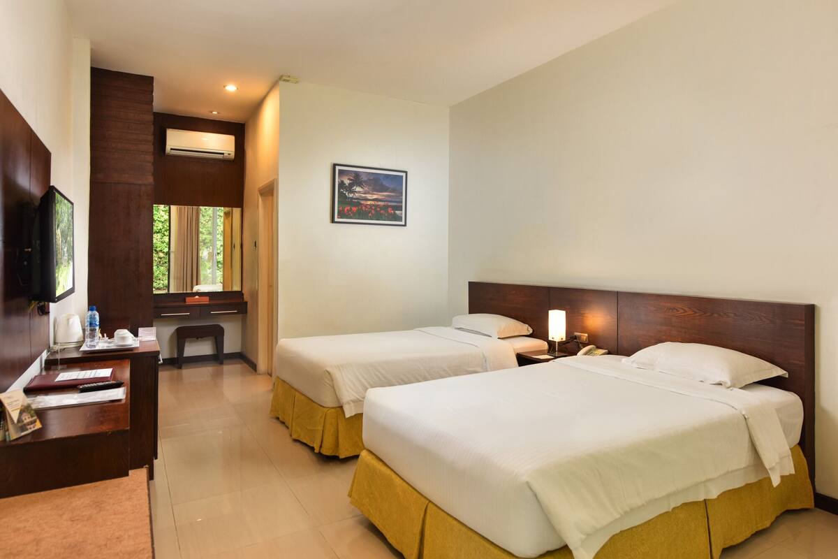 A hotel room with two beds, a desk with a telephone, a television, and a window with curtains.