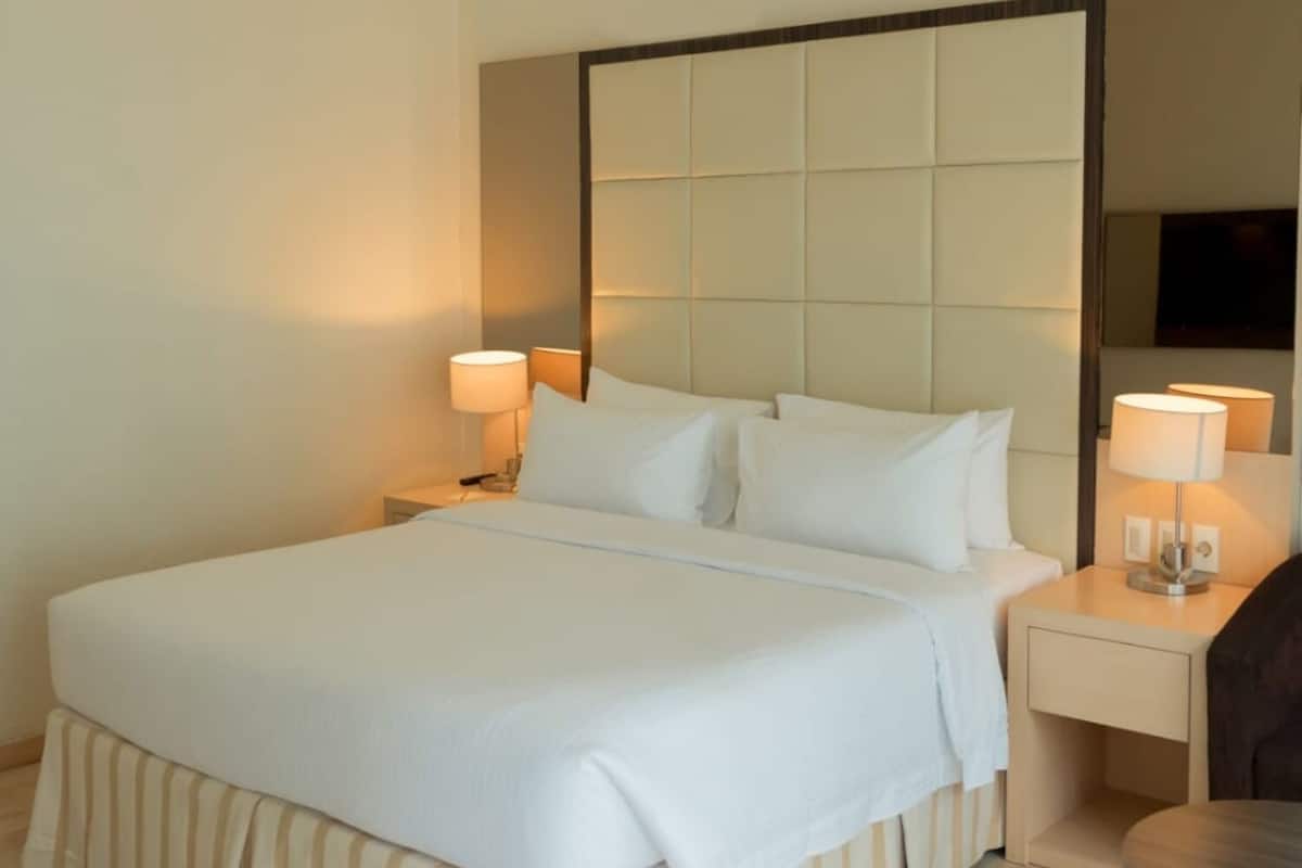 A hotel room with a large bed, two bedside tables with lamps, a round table, and a large mirror on the wall.