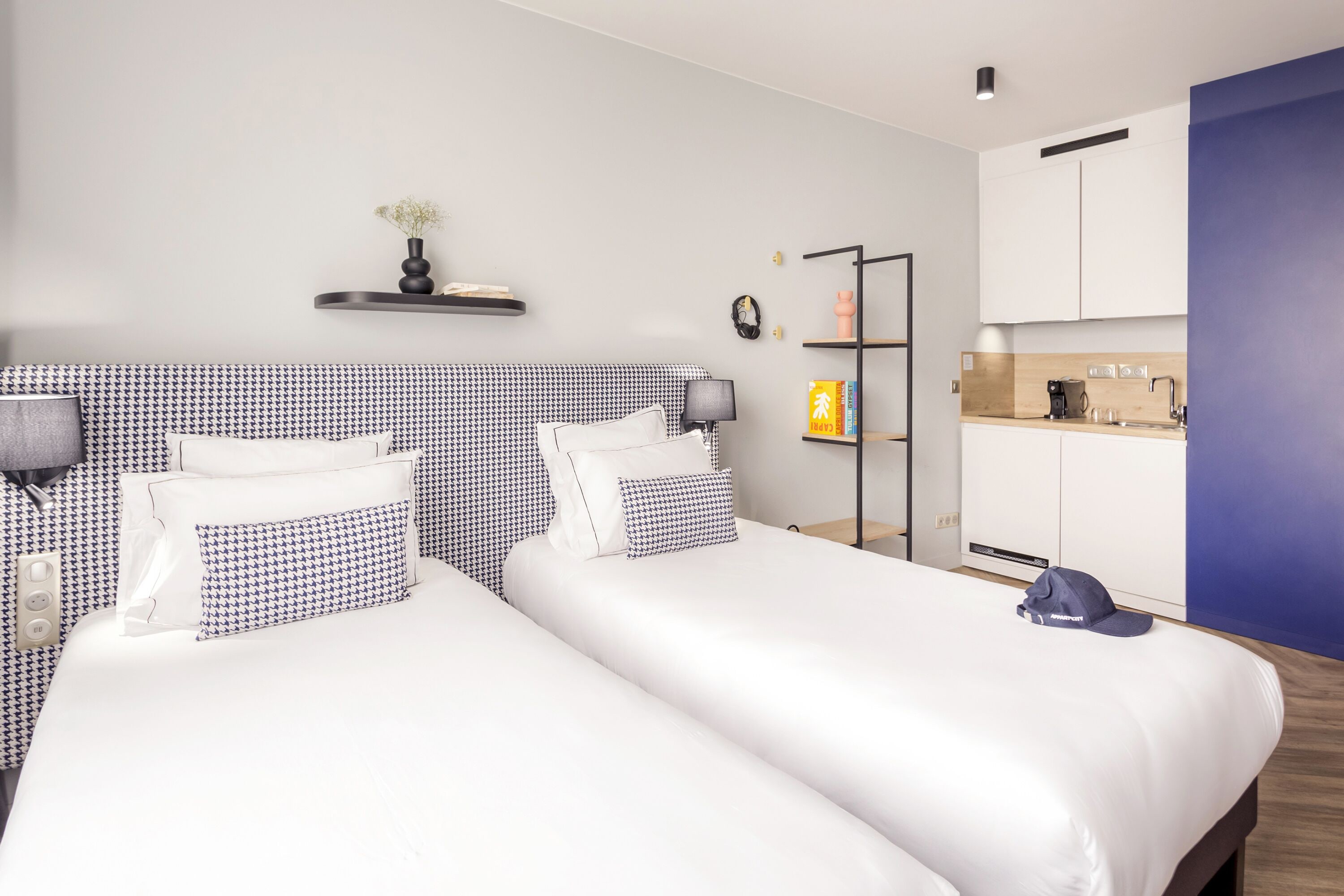 Une chambre d’hôtel avec deux lits, une petite kitchenette et un mur d’accent bleu.