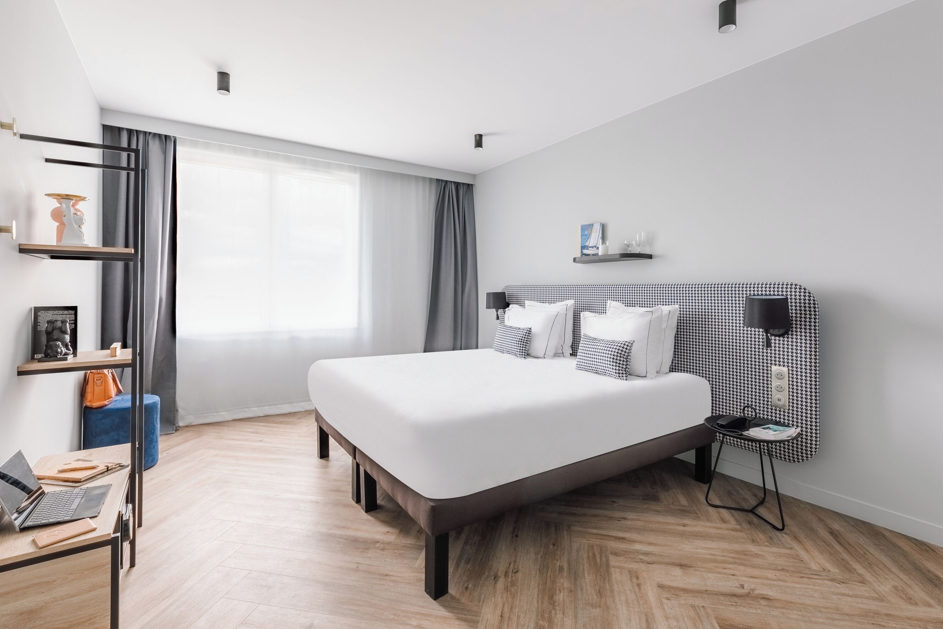 Une chambre d’hôtel moderne avec un grand lit, un bureau avec un ordinateur portable, une petite table d’appoint et une fenêtre avec des rideaux.