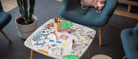 A small table with a colorful drawing pad, a cactus plant, a teddy bear, and a blue chair.