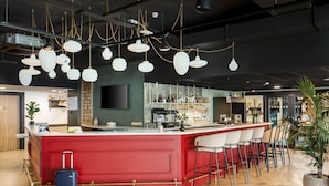 Zona de bar moderna con mostrador rojo, varias lámparas colgantes y disposición de taburetes.