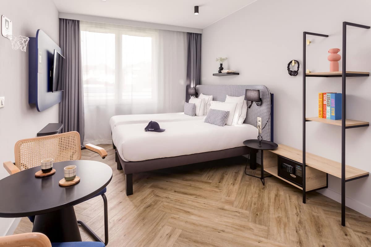 Habitació d'hotel moderna amb llit, escriptori, cadira, televisió i prestatgeria.