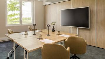 Un salón de conferencias con una gran mesa, cuatro sillas, una pantalla de proyector y una ventana que da a árboles.