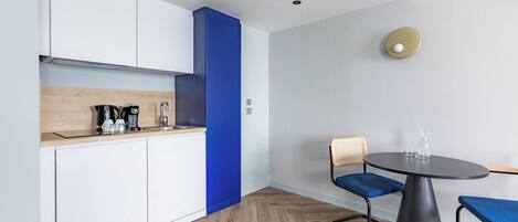 A modern kitchen with white cabinets, a blue accent wall, and a round dining table with blue chairs.
