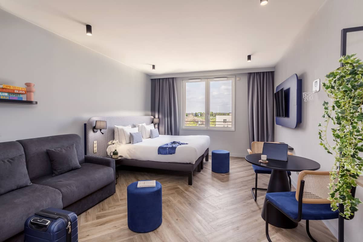 Habitació d'hotel moderna amb llit, sofà, escriptori i finestra gran.