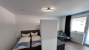 Une chambre à coucher moderne avec un lit, une table de chevet et un petit coin salon comprenant une chaise et une table.