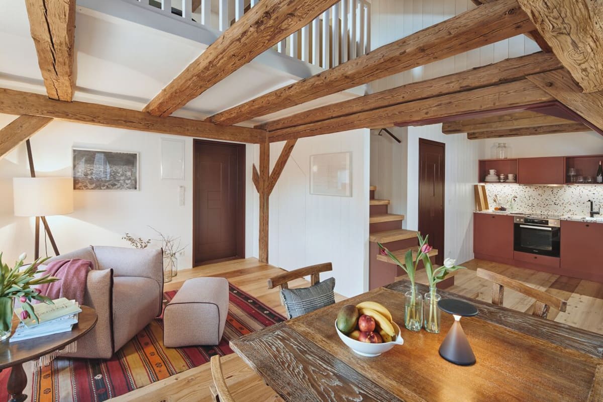 A spacious loft with exposed wooden beams, a dining area with a wooden table, and a kitchen with modern appliances.